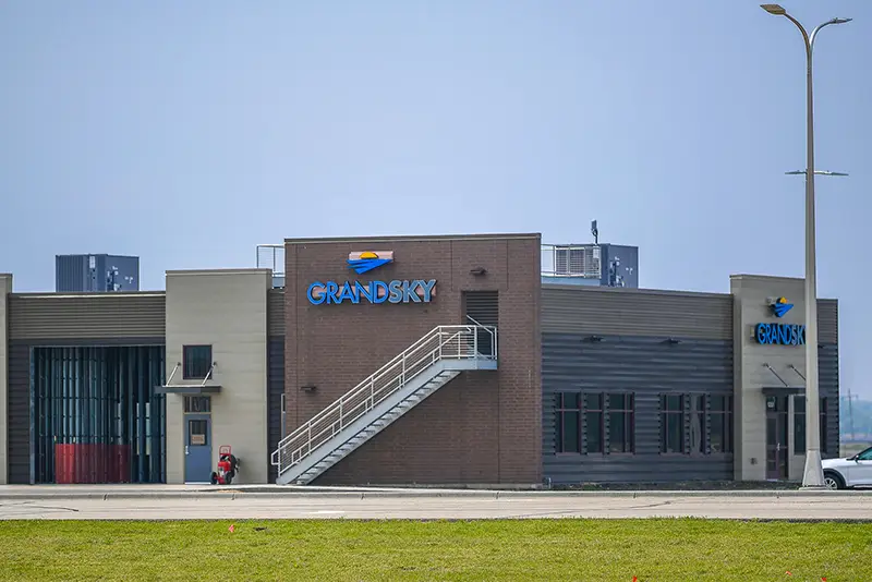 Exterior of the Grand Sky building with blue signage, an outdoor staircase, and open hangar door under a clear sky.