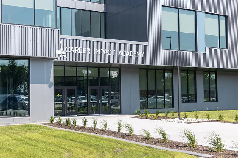 The modern exterior entrance of Career Impact Academy at 4201 Career Drive, featuring dark metal panel siding, large glass doors, and freshly landscaped grounds.
